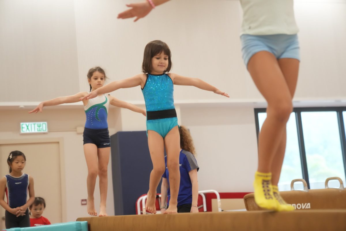 Children wearing party hats laughing while sitting on colorful gymnastics mats with balloons.