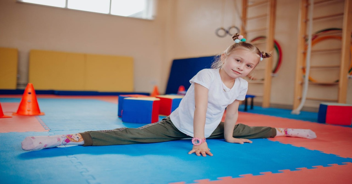 A rhythmic gymnastics student gracefully swirling a long pink ribbon in a brightly lit studio.
