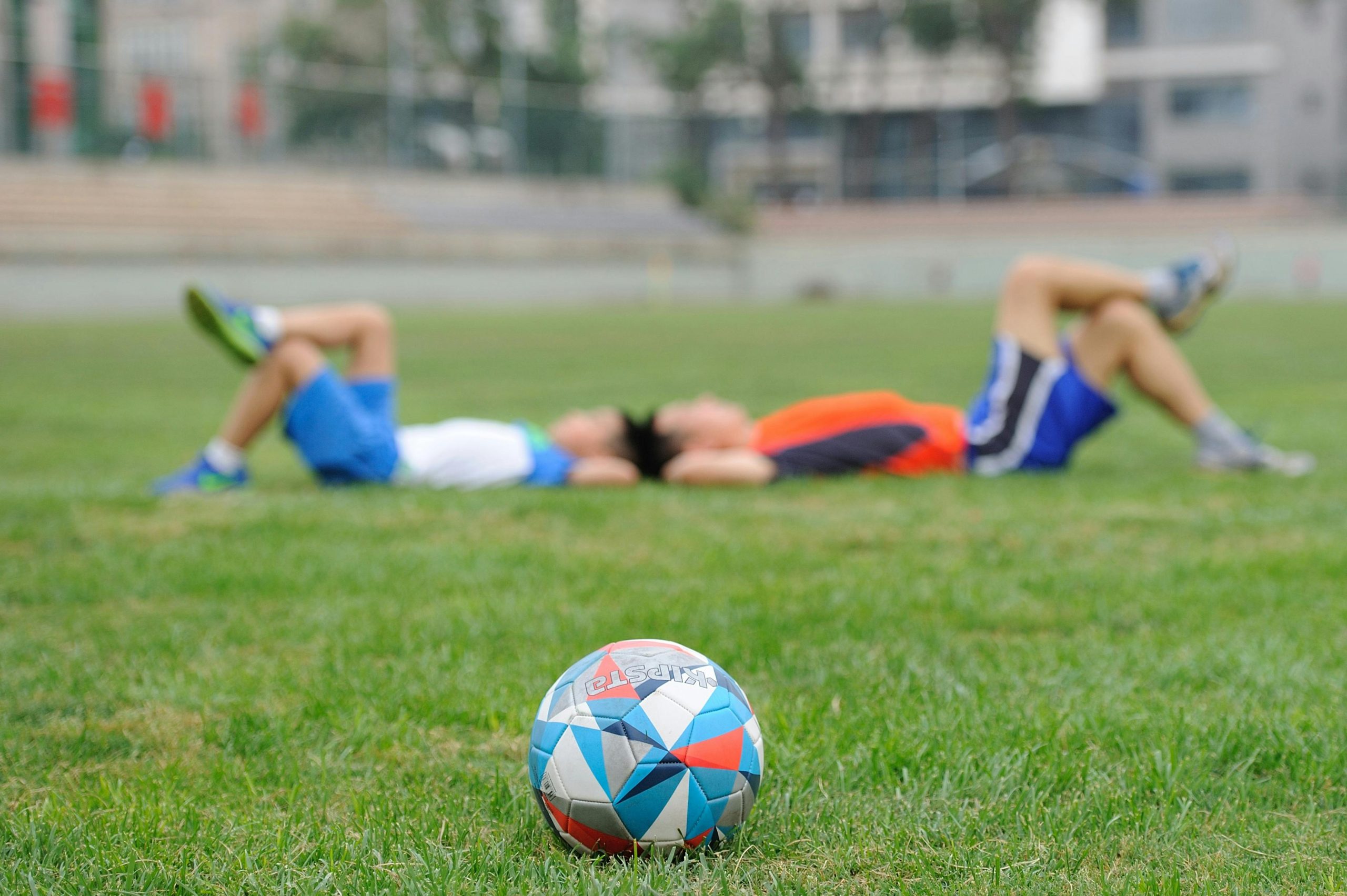 Two young teammates in uniforms hugging after a game on a grassy field.