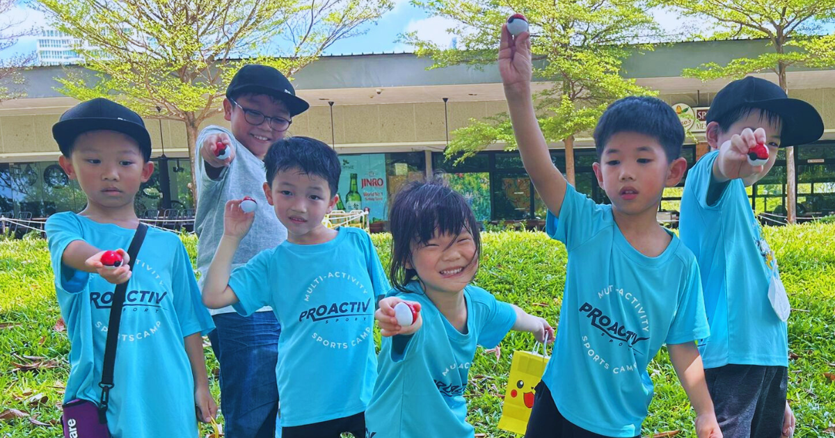 Large group of children in colorful ProActiv Sports shirts cheering with their coaches at a summer camp.