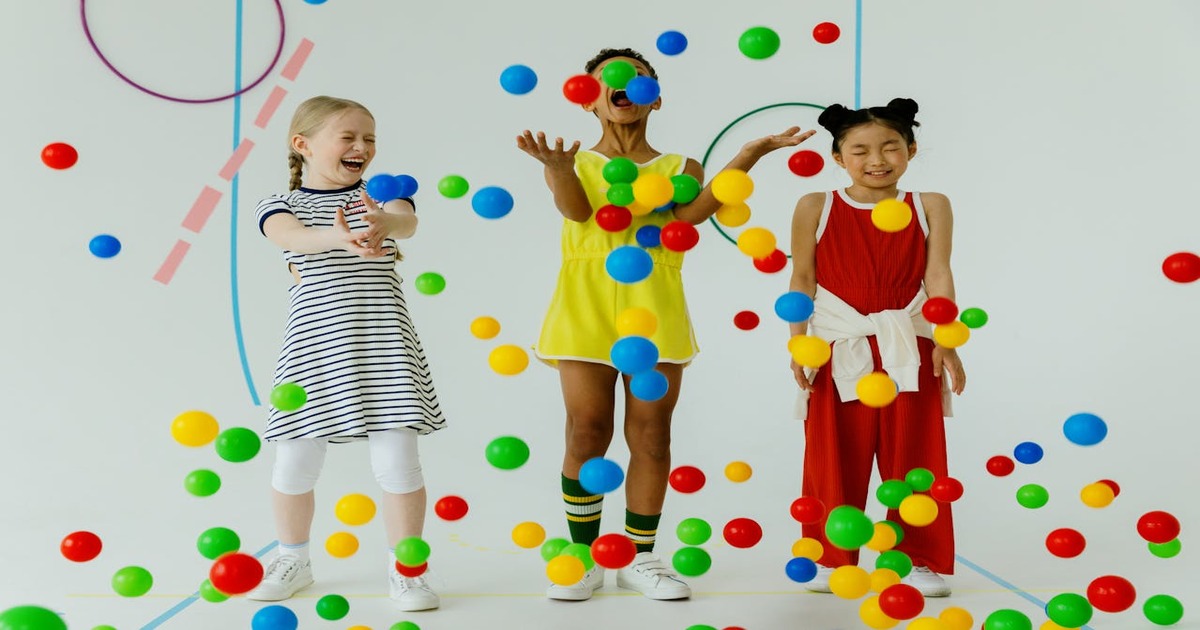 Children wearing birthday hats playing on colorful foam gymnastics blocks and mats.